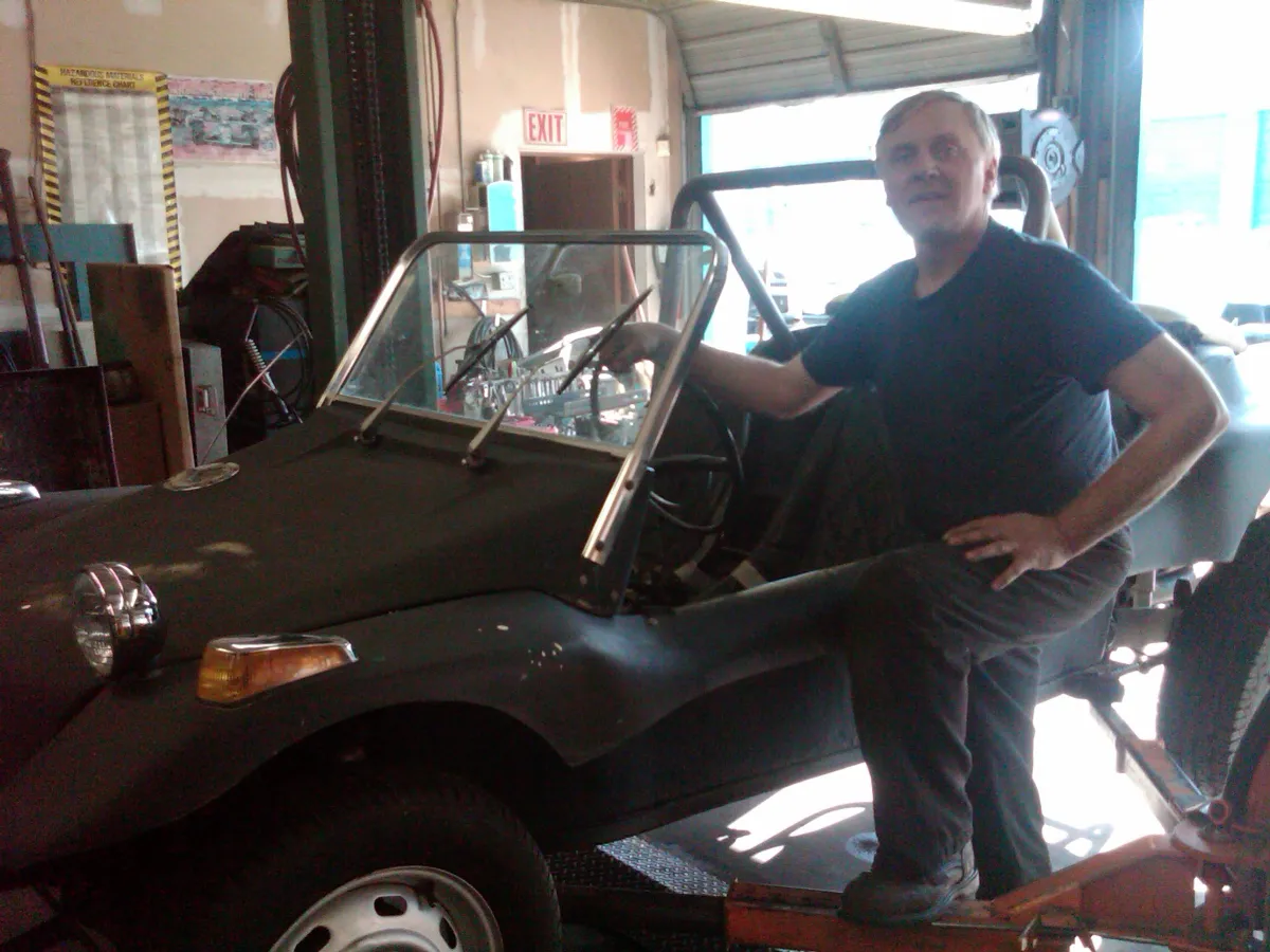 Ed leaning on the bare tube frame of a dune buggy inside the shop, body panels removed