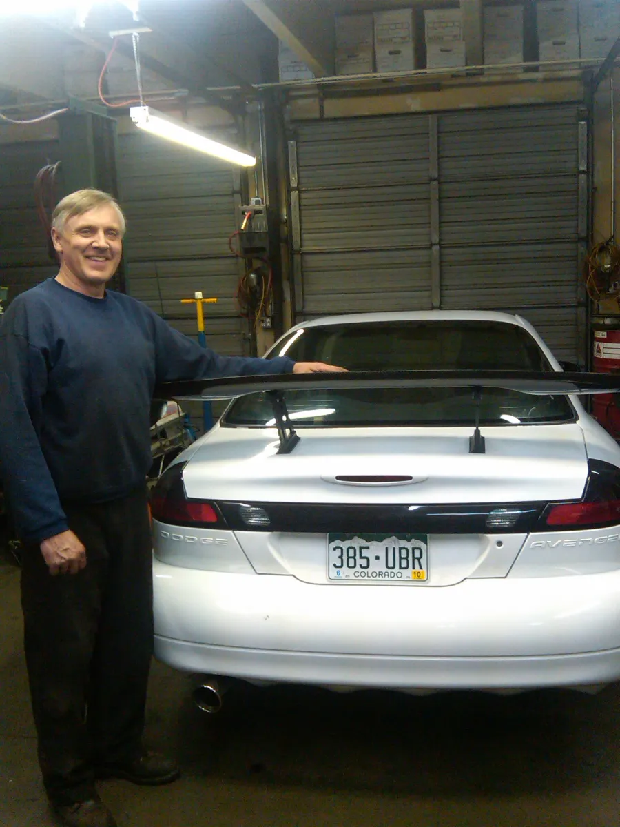 Ed standing beside a white sports coupe with a rear spoiler, outside the shop in winter, around 2010