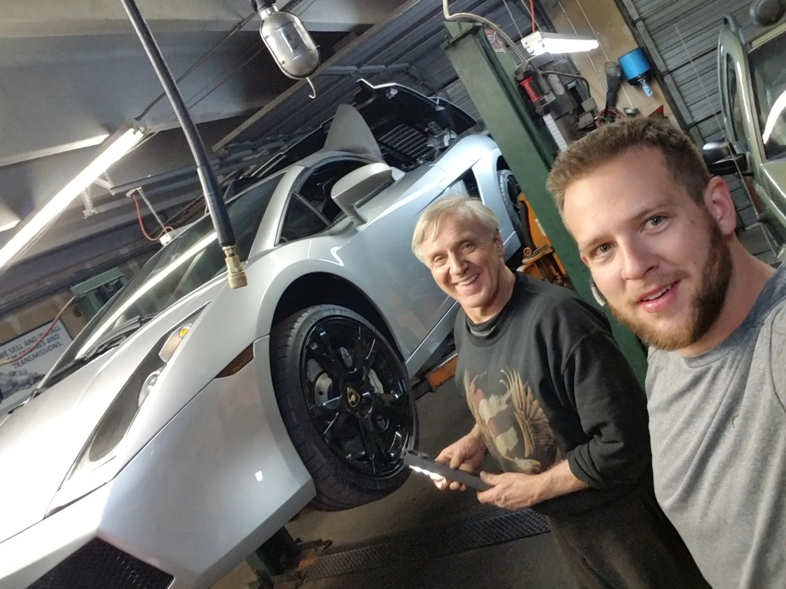 Ed and his son Matt smiling in the shop beside a silver Lamborghini Gallardo raised on the two-post lift