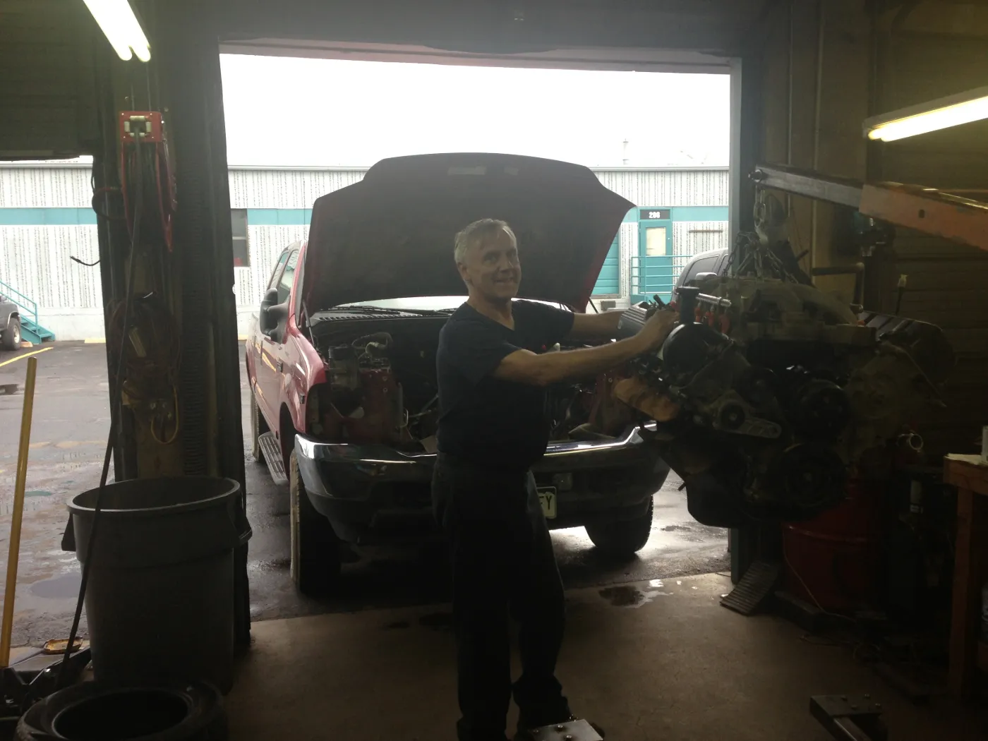 Ed working at an engine on a stand in the open roll-up doorway of the shop