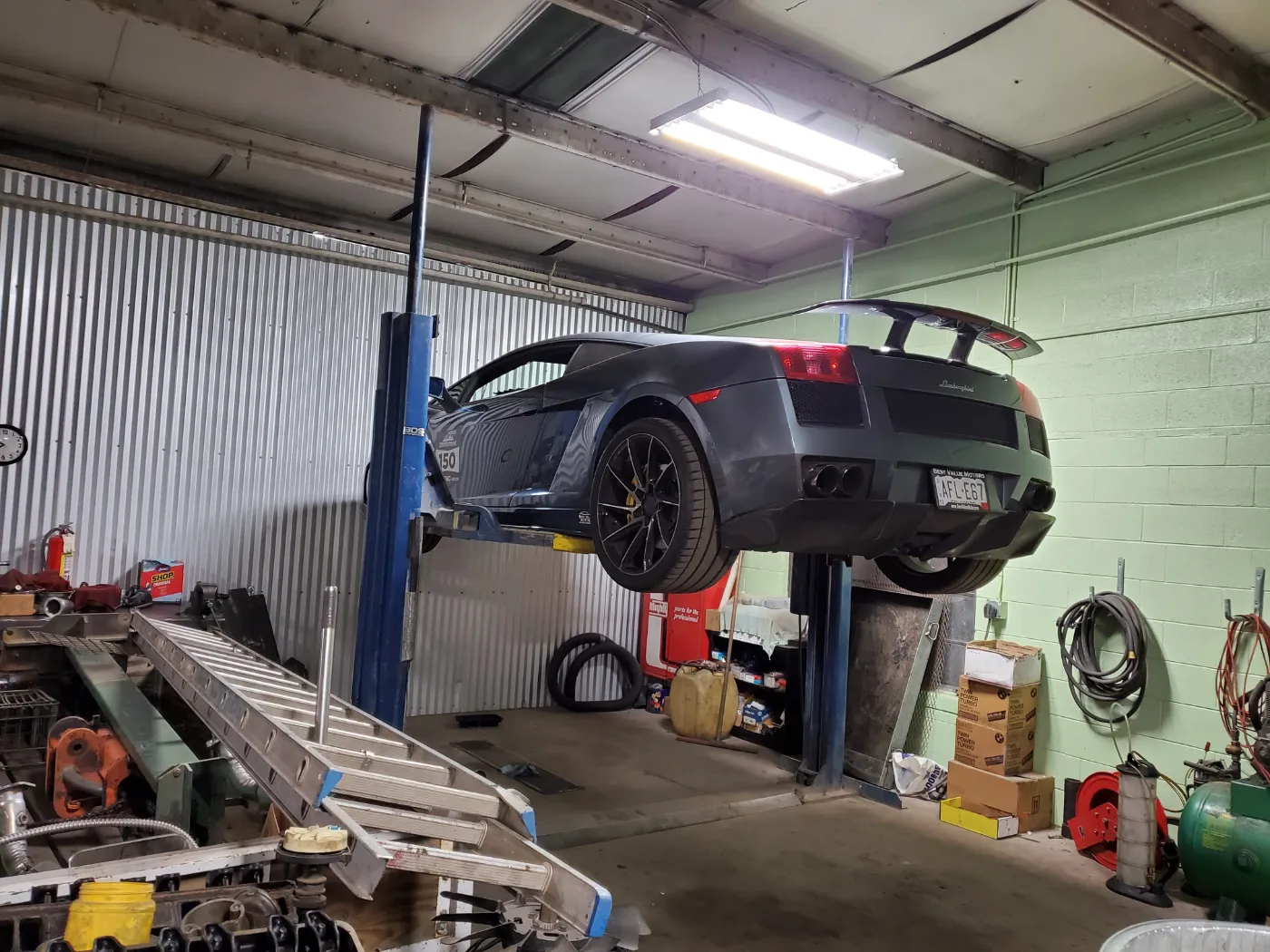 A grey Lamborghini Gallardo raised on the two-post lift, seen from behind