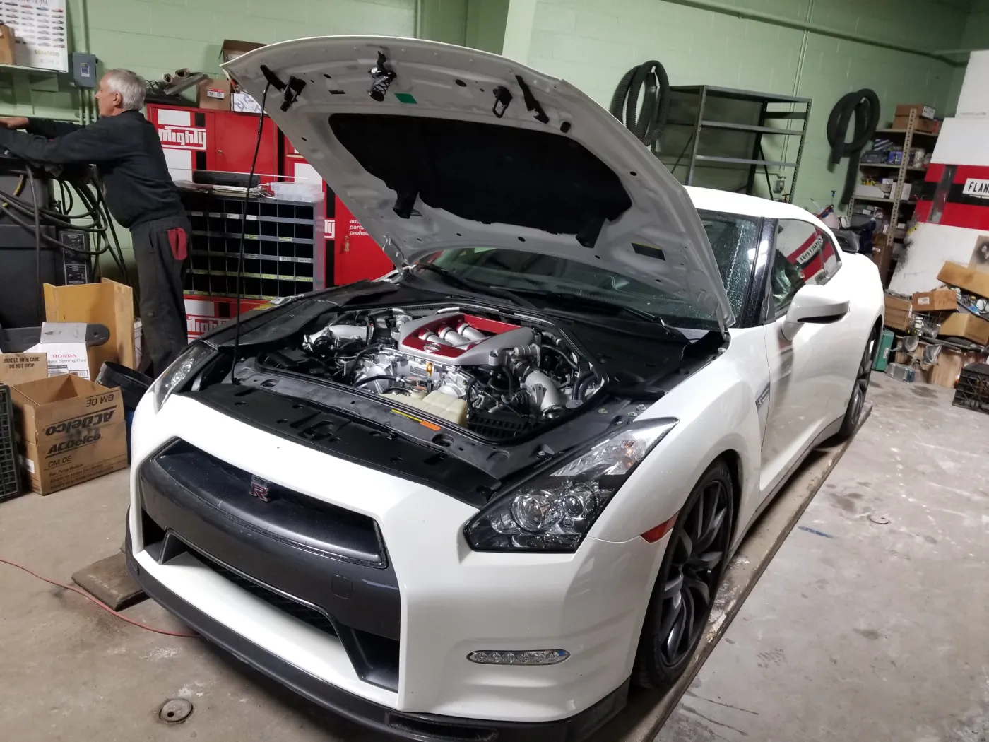 A white Nissan GT-R inside the shop with its hood raised and the twin-turbo V6 exposed