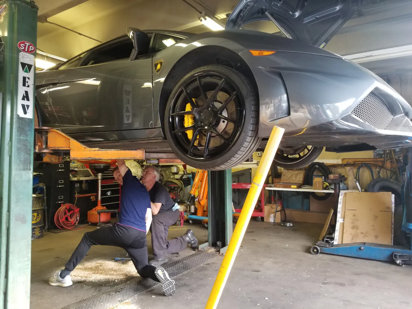 Ed kneeling underneath a grey Lamborghini Gallardo raised on the lift, working on its underside