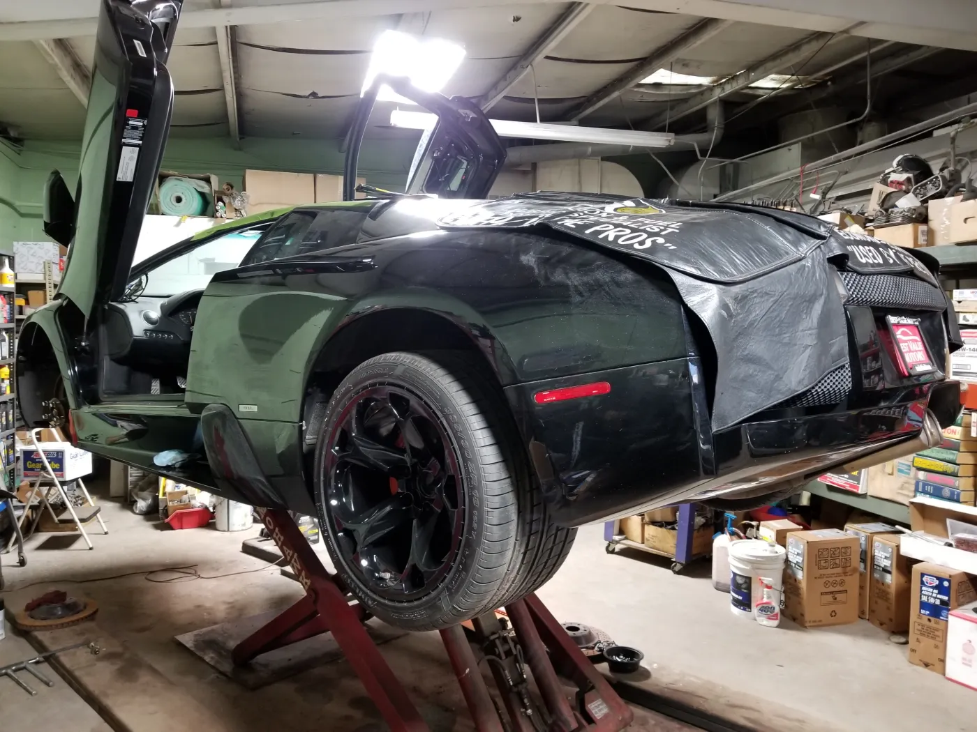 A dark Lamborghini Murcielago on jack stands with one scissor door raised and body panels removed