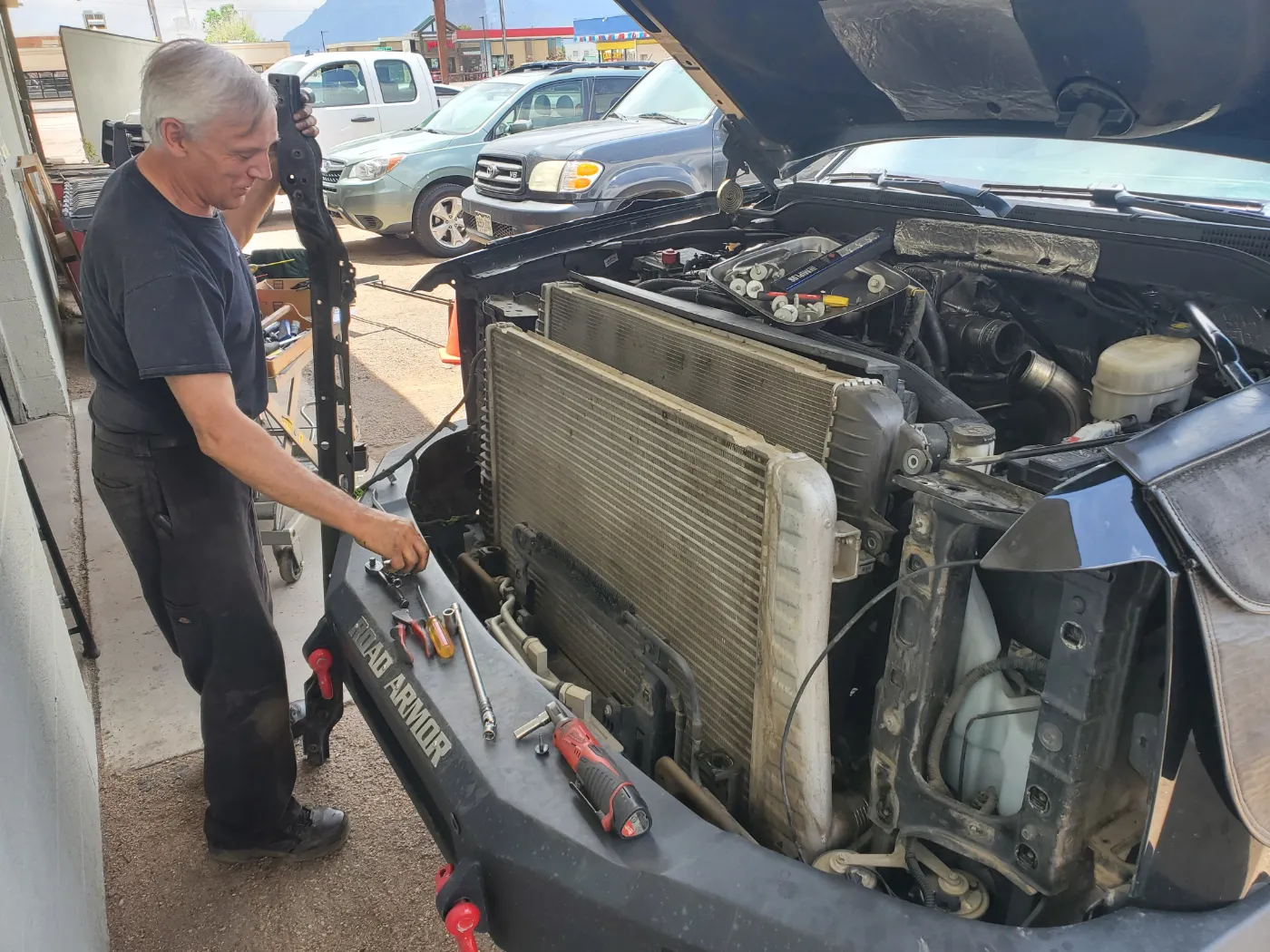 Ed working on the front of a car with the hood up and the radiator and condenser stack exposed